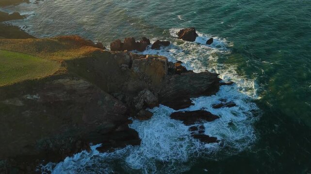 Aerial drone flying forward above coastal shoreline with ocean waves and greenish water along the coast of Spain
