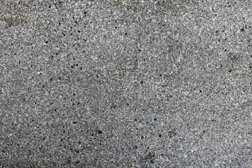 Full-frame close-up of a dark, speckled stone or asphalt texture. Rough, grainy surface background.