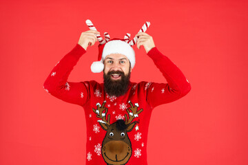 happy brutal hipster man in santa hat with party decoration on red background, christmas