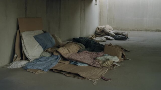 Makeshift bedding and cardboard on a cold, concrete floor in a dimly lit, stark room, evoking poverty, homelessness, and the raw reality of desperate living conditions
