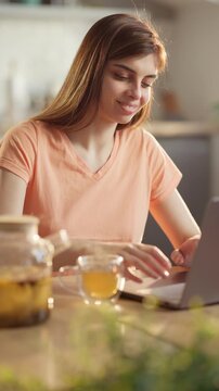 morning online work with citrus tea at sunlit kitchen woman smiles at phone chat then starts working on laptop wellness lifestyle calm routine self care balance real time vertical video