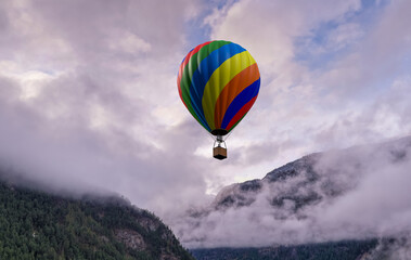 Fototapeta premium Colorful Hot Air Balloon Floating Over Mountain Clouds in BC Landscape