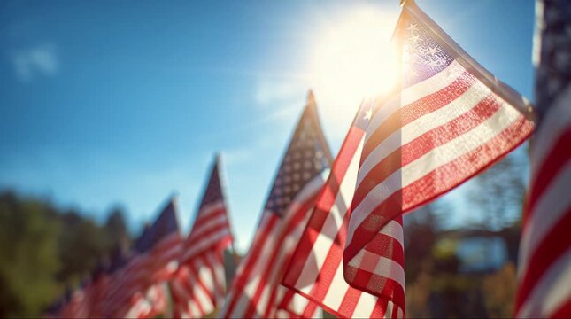 Row of American flags waving in the wind under a bright sunny sky with lens flare.