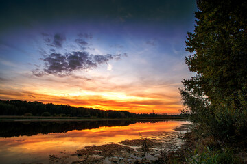 Beautiful summer sunset and colorful sky over the lake. Clouds are reflected in the calm water. Beauty in this world