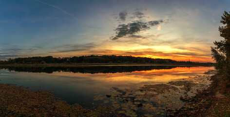 Beautiful summer sunset and colorful sky over the lake. Clouds are reflected in the calm water. Beauty in this world