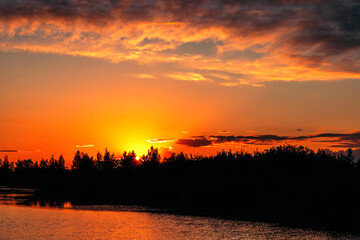 Beautiful summer sunset and colorful sky over the lake. Clouds are reflected in the calm water. Beauty in this world