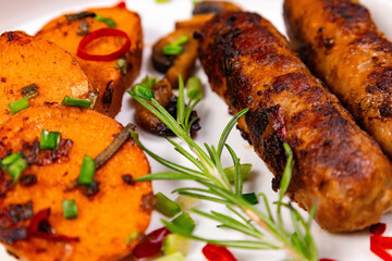 Sausages and sweet potatoes served on a white plate with garnishes in the kitchen during dinner time