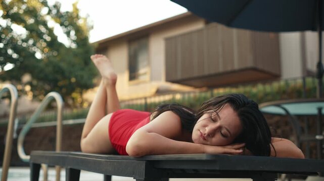Girl in red swimsuit lying on poolside sunbed and taking a nap