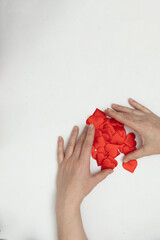 Two hands are sorting through a pile of small red hearts on a plain white surface. This scene shows preparation for Valentine's Day themed digital content.