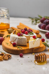Brie cheese on a board with walnuts, honey and berries