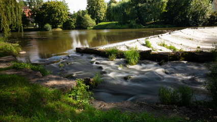 Fototapeta premium Lush Green River Landscape with a Small Weir and Overhanging Trees