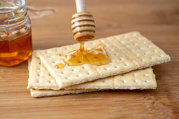 Close-up of golden honey dripping from a wooden honey dipper onto crisp crackers placed on a...