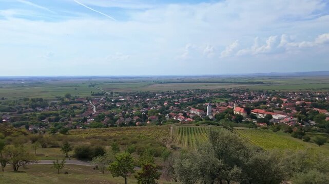 A panoramic view of Tarcal, Hungary, as the camera pans right, revealing the village, Tokaj-hegyalja vineyards, rolling fields, and a tranquil countryside under a clear autumn sky.