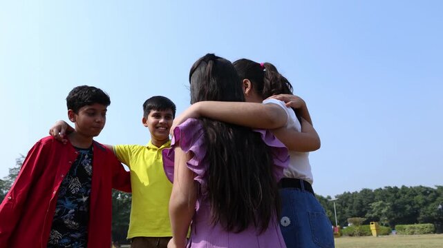 Happy group of indian kids friends embracing and sharing a candid conversation together in summer park, concept of teamwork and friendship. Children having fun talking and discussing outdoor.
