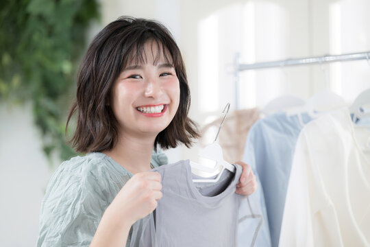 洋服を手に取り笑顔で選ぶ若い女性のガーリーなファッションライフスタイル　カメラ目線のクローズアップ