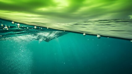 Underwater view of the ocean surface with green clouds and sunbeams piercing through the water.