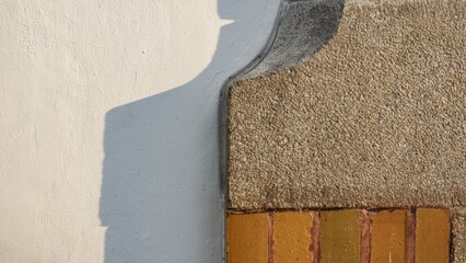 Architectural close-up of a building's exterior featuring a white plastered wall meeting a textured stone block and yellow brick accents under sharp, natural geometric shadows.