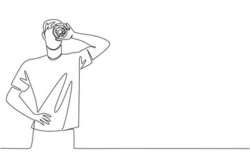 Continuous line drawing of a man holding a donut in front of his eye, highlighting playful enjoyment and food culture in a minimalist concept for National Donut Day.