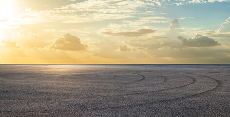 Empty asphalt race track road with tire tracks and beautiful sky clouds at sunset