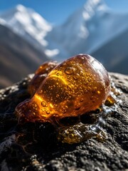 mountain landscape in, Dark brown Shilajit resin oozes from cracks in rugged Himalayan rock surface. Golden undertones glisten on the earthy mineral deposit. Majestic snowy mountains rise in backgroun