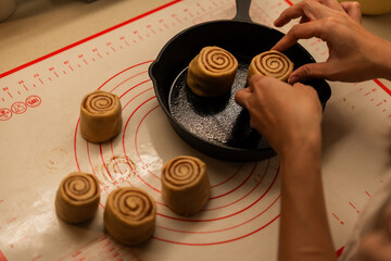 Person places cinnamon roll dough into a dark cast iron skillet on a measuring mat surface