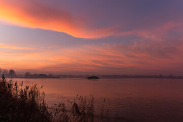 Spokojny, różowy wschód słońca z miękkimi chmurami nad spokojną wodą, delikatnymi odbiciami i pogodną poranną atmosferą. © Elżbieta Kaps