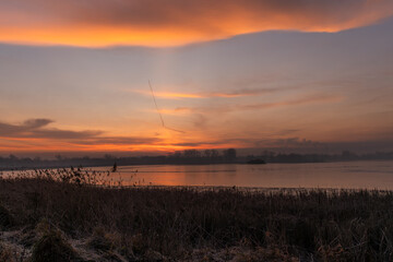 Spokojny, różowy wschód słońca z miękkimi chmurami nad spokojną wodą, delikatnymi odbiciami i pogodną poranną atmosferą. © Elżbieta Kaps