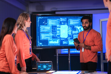 In a government command center, a diverse team of intelligence analysts collaborates on a critical...