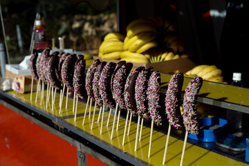 The bananaes coated by the chocolate holding on the wooden stick for selling