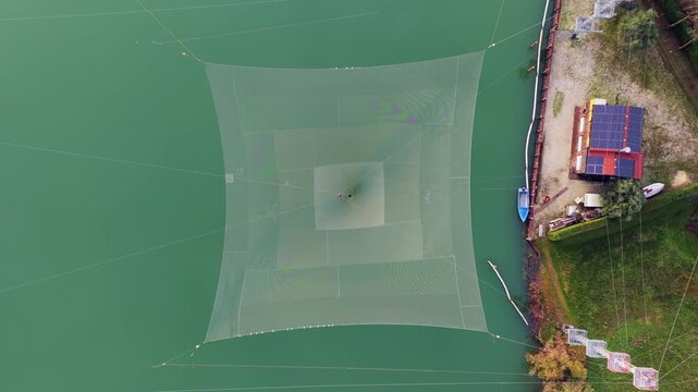 drone jesolo top-down view of a square fishing net submerged in green river water. Artistic aerial drone shot highlighting the geometry and textures of traditional fishing equipment