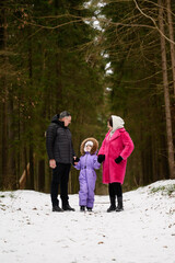 Fototapeta premium Parents and daughter are walking along path in snowy forest, holding hands and looking at each other with love. Family enjoys walk through beautiful winter forest