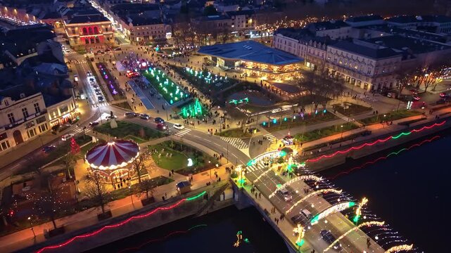 Aerial drone view of the Lumi&egrave;res de Laval festival at night. Features the illuminated Place du 11 Novembre with a carousel, festive light sculptures and traffic on the Aristide Briand bridge, France