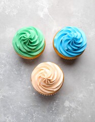 Pastel Swirl Cupcakes: Green, Blue, and Peach Frosting on a Textured Gray Surface