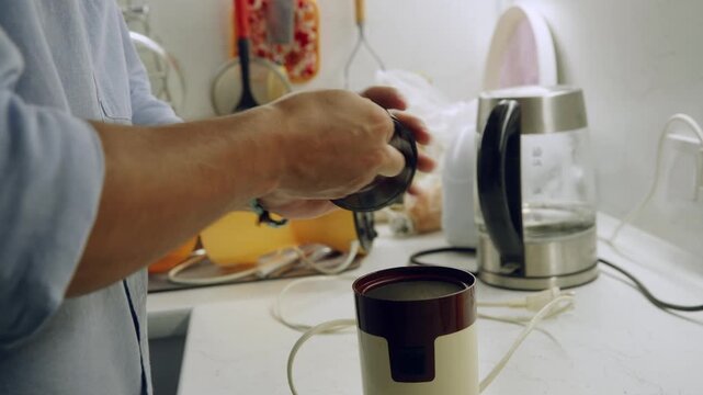 Person holding black coffee capsule near modern coffee maker with dark brown cup on white countertop. Contemporary kitchen scene symbolizing morning caffeine ritual and home beverage preparation.
