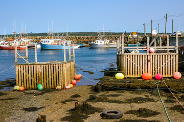 Colorful lobster boats sit at low tide in the fishing harbour on Brier Island, Nova Scotia, with wooden docks, buoys, and calm coastal waters under a clear summer sky.