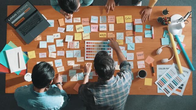 Time lapse of business team with casual outfit looking laptop screen and sharing idea. Aerial view of manager working and checking color palette at table with sticky notes and headphone. Symposium.