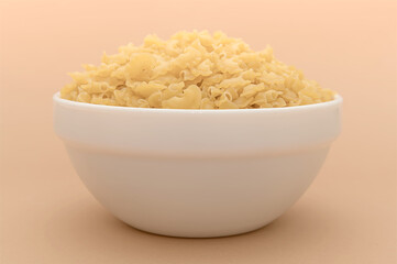 Dry yellow pasta in a white plate on a beige background.