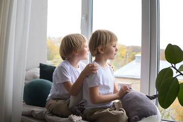children, blonde twin boys, look out the window, sitting on the window sill