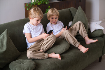 kids blonde boys twins using smartphones on the couch in living room