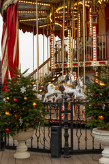 Fototapeta premium Carousel with white horses and decorated tree at festive market