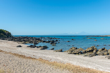 岩礁が広がる海岸と穏やかな海、遠くに富士山を望む風景