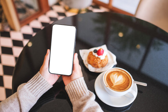 Top view mockup image of a woman holding and using mobile phone with blank desktop screen in cafe