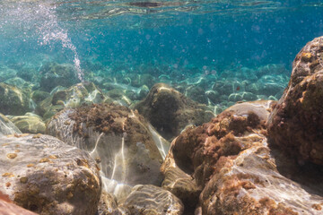 Underwater view of sunbeams reflecting on rocky seabed with clear turquoise water and bubbles in the Mediterranean Sea, Nice, France