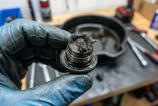 Mechanic holding magnetic oil drain plug covered in metal shavings during car engine oil change
