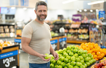 Man shops for fresh apples at a market. Customer chooses organic apples in a grocery store. A male buyer examines raw apples in the produce section of a supermarket. Healthy fruits at grocery store.