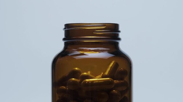 Amber supplement bottle rotates slowly as capsules drop inside, clean studio closeup for pharmacy marketing and wellness ads.