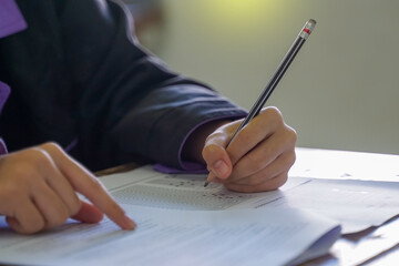 Students sitting at desks in a classroom, focused on writing and completing their examination papers or tests during a school lesson.
