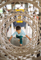 Asian Little Boy Crawling Through Rope Tunnel Playground, Active Child Developing Motor Skills