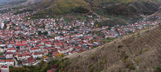 Aerial view of residential neighbourhoods in Pogradec, Albania, set against rolling hills with autumn vegetation and dense urban housing.