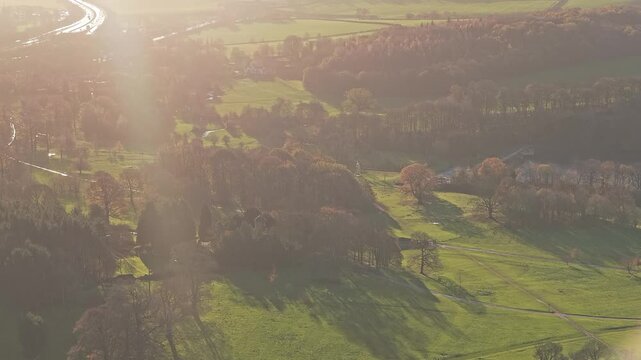 A sweeping high-angle view contrasting a large, busy arterial road with the protected, undulating autumnal forests and fields surrounding a major cultural park near Yorkshire Sculpture Park